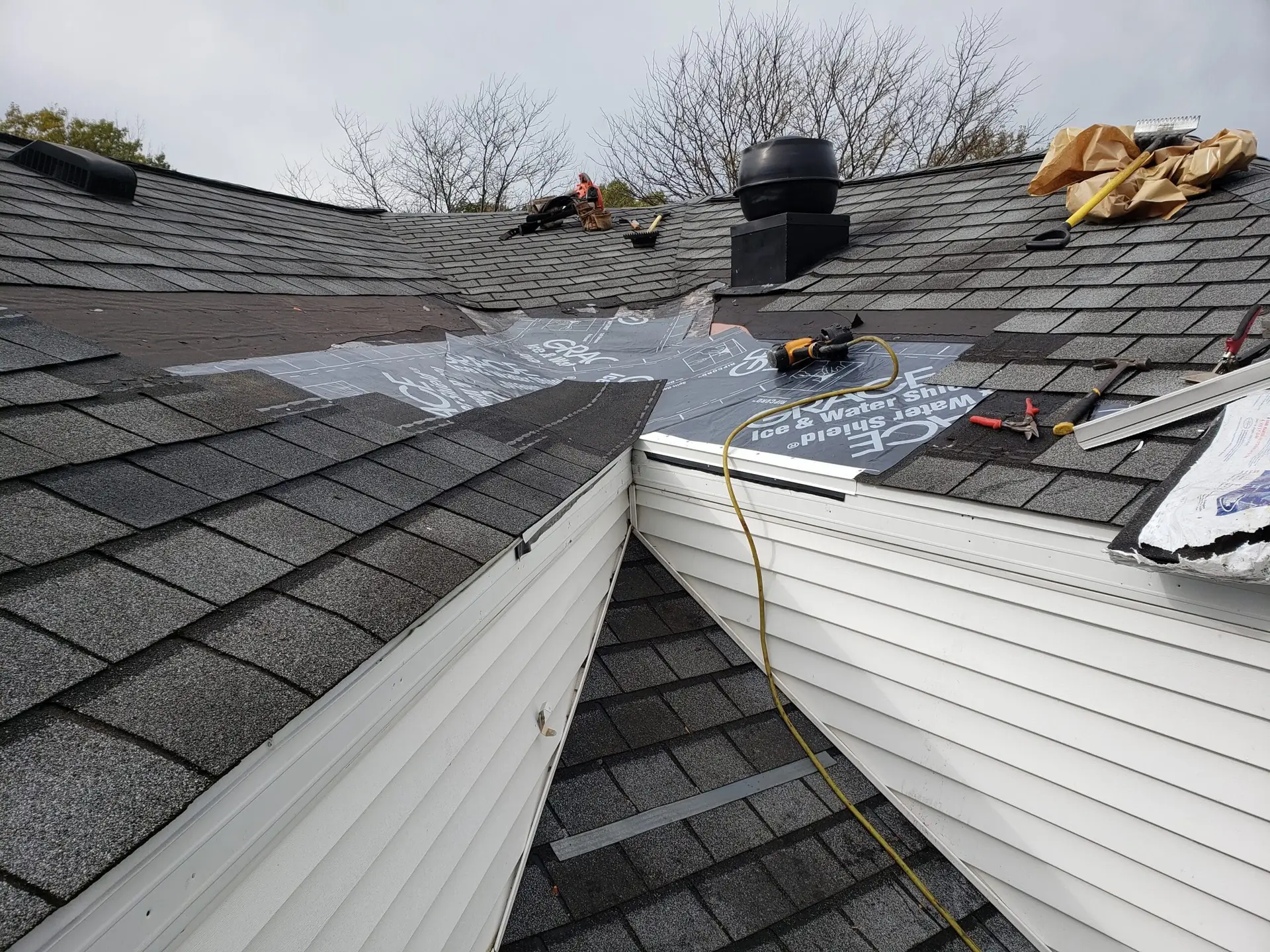 A section of a roof under repair with construction materials, tools, and a water and ice shield visible. The roof is partially shingled, with some parts exposed, all carefully handled by professionals specializing in exterior construction Erie PA.